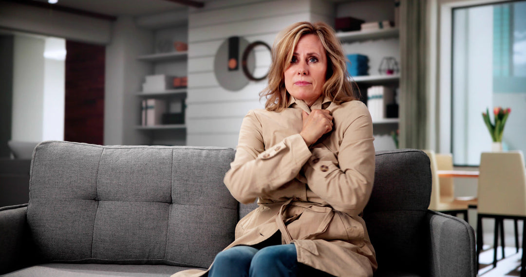 Women in a living room feeling cold with Cold Flashes sitting on a sofa covering herself with her coat.