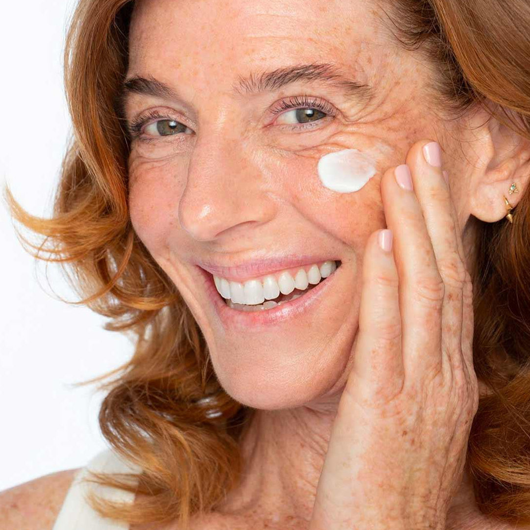 Woman applying Dew As I Do moisturizer to her cheek for hydrated, youthful, and radiant skin.