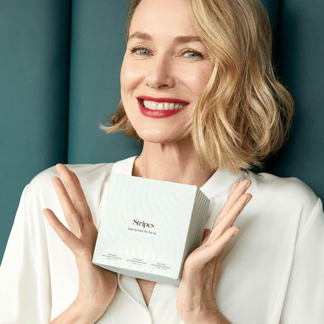 Smiling woman holding the Glow Up From The Toe Up skincare box featuring hydration products for skin from head to toe.