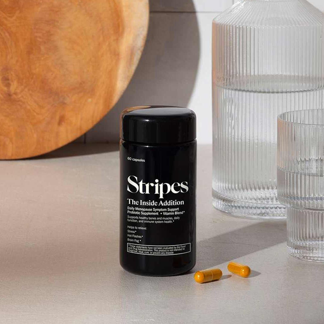 Black bottle of The Inside Addition supplement with capsules beside glass water on countertop