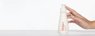 Hand holding a Oh My Glide white bottle labeled 'Stripes' on a light background