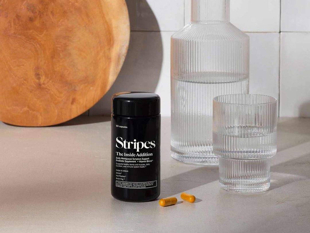 Menopause Survival Kit showing supplement bottle, two capsules, and a glass of water on kitchen counter.