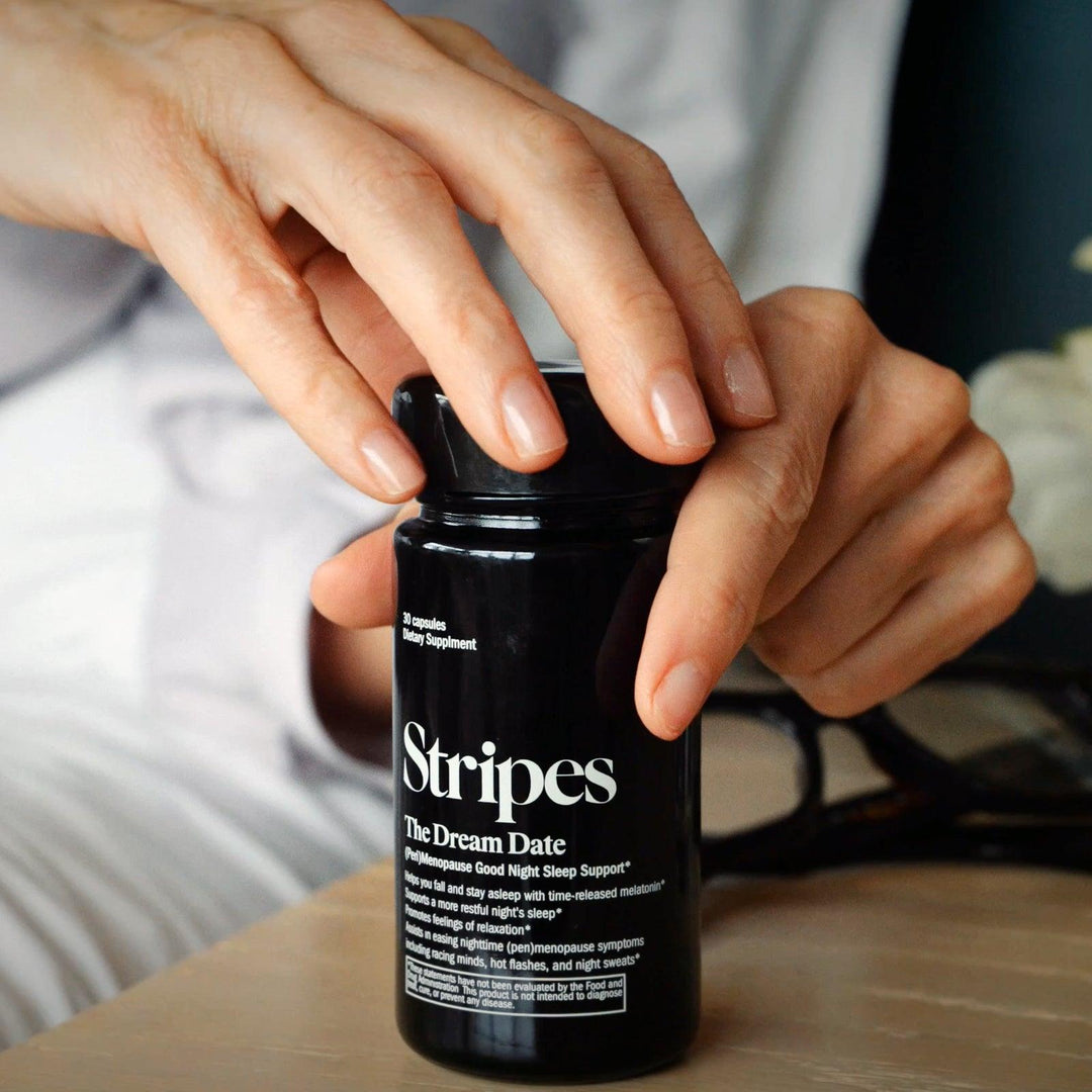 Close-up of hands opening a black bottle of Stripes The Dream Date supplement for good sleep support.