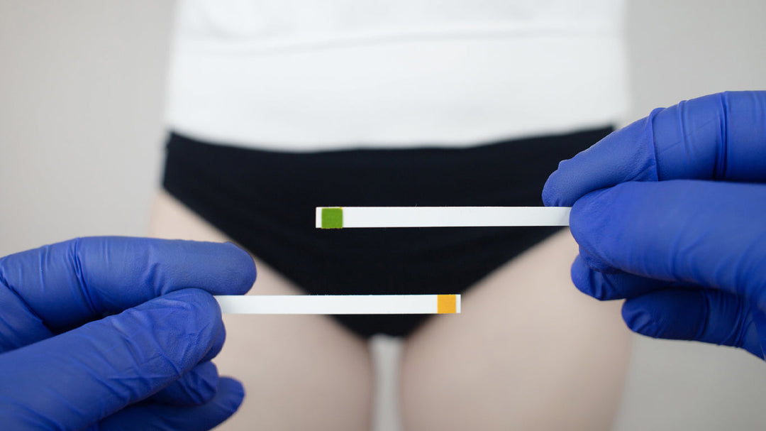 Hand with blue plastics gloves in from of a women inher underwera holding two PH testing sticks for PH balance tests.