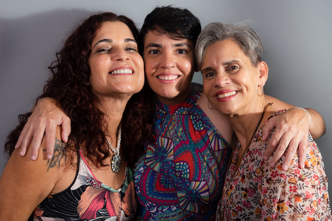 Three latina women posing together with a gray background