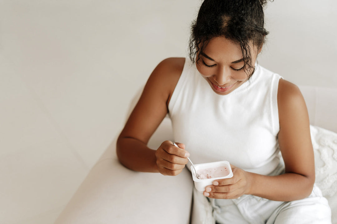 Young woman smiles while eating yogurt from a single serving container at home