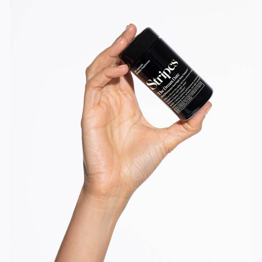 Hand holding a black container labeled 'Stripes' against a white background