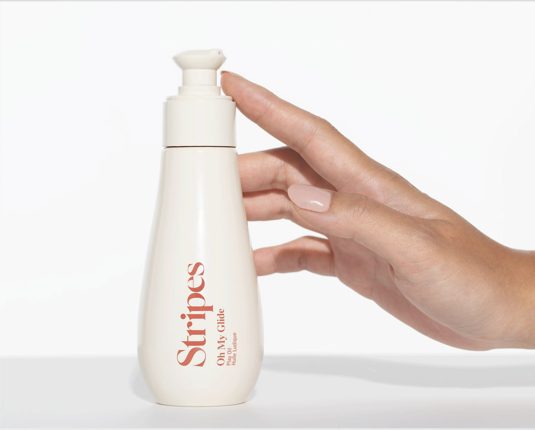 Hand holding a Oh My Glide white bottle labeled 'Stripes' on a light background