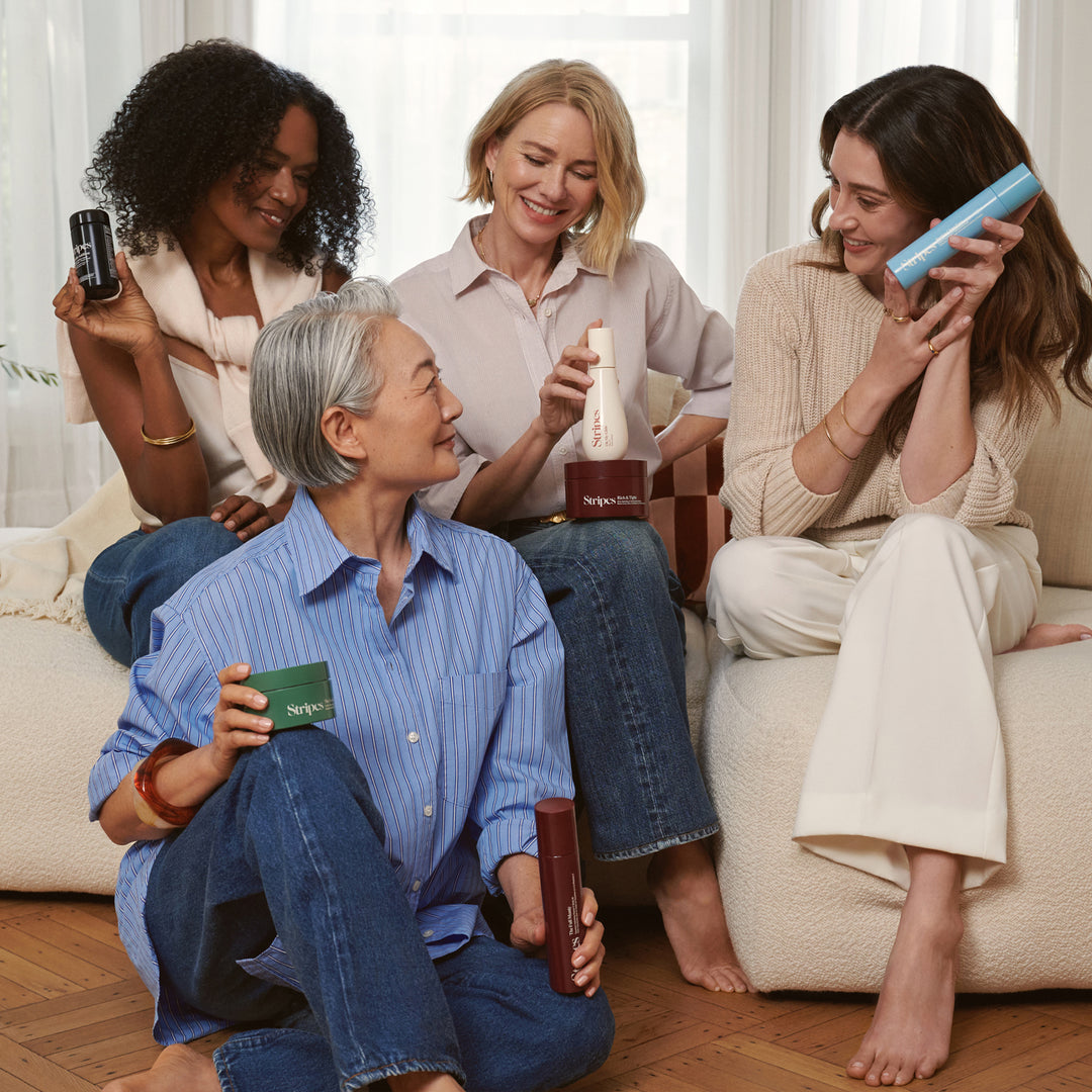 Four women, including Naomi Watts, are sitting on a couch holding various hair care products.