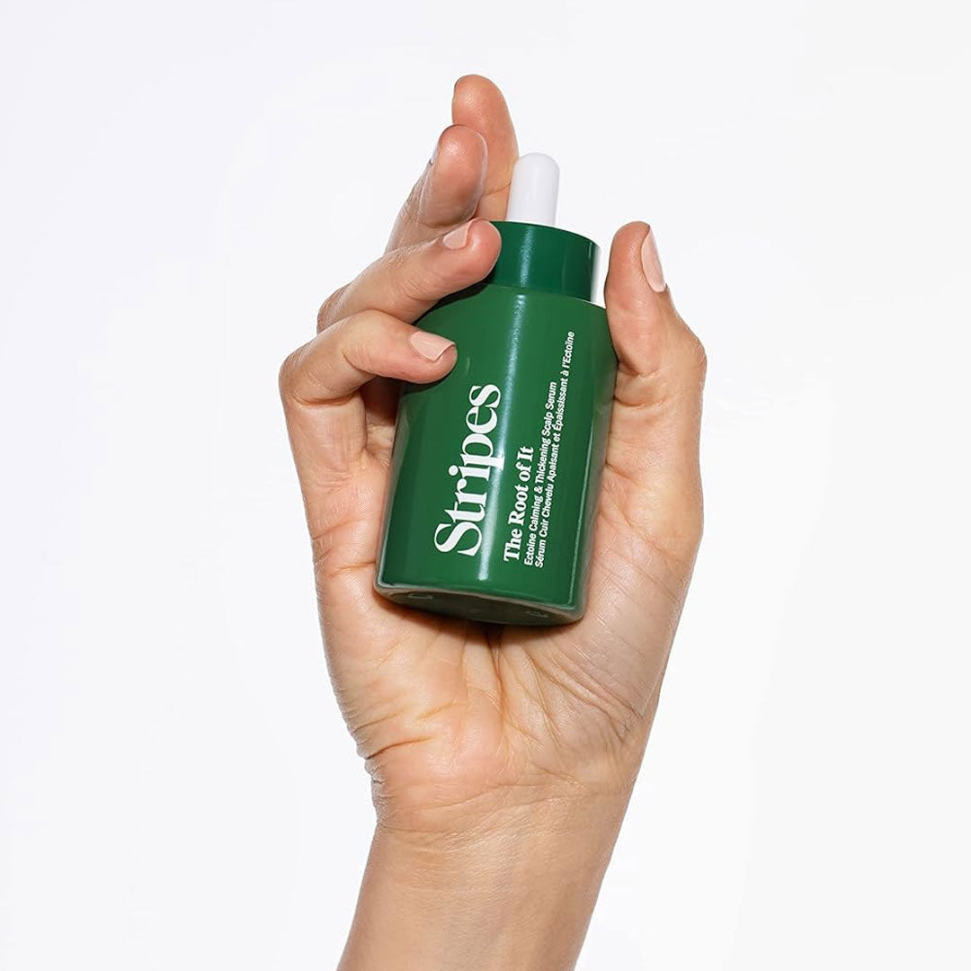 Hand holding a green bottle of Stripes The Root Of It scalp serum for thickening and hydrating hair.
