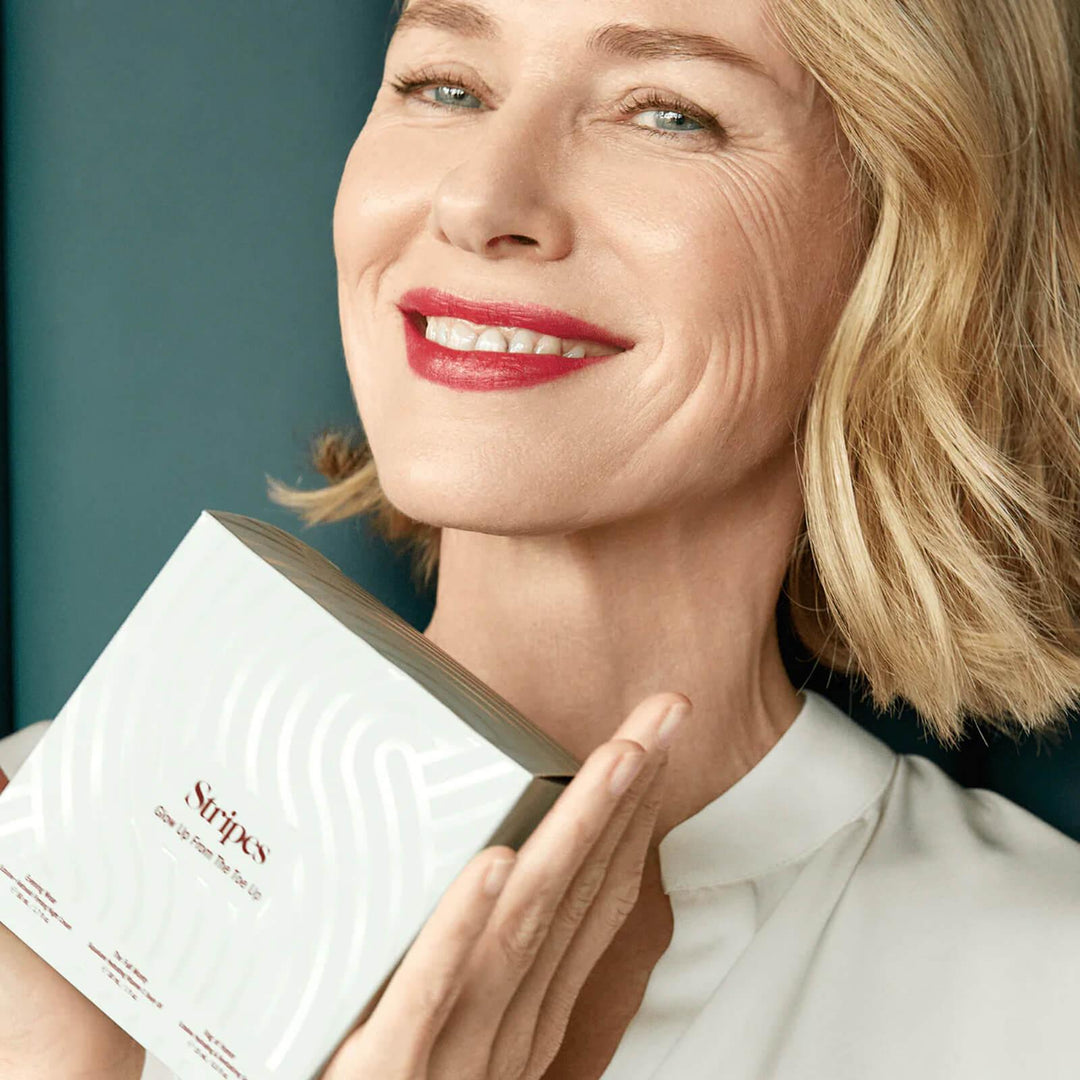Woman smiling and holding Glow Up From The Toe Up skincare box for hydration and skin rejuvenation.