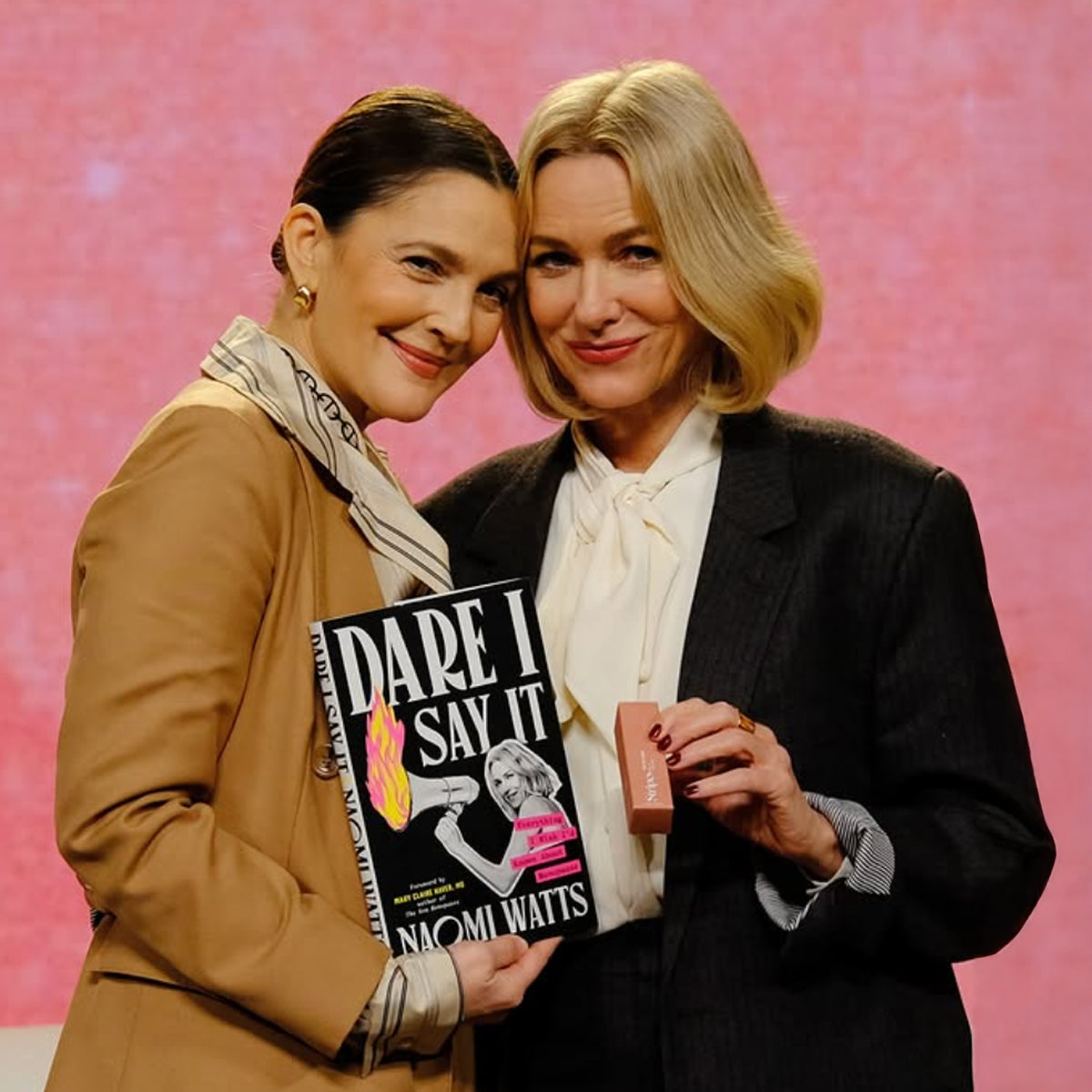 Drew Barrymore and Naomi Watts posing in front of camera with Dare I say it book and a Stripes Product