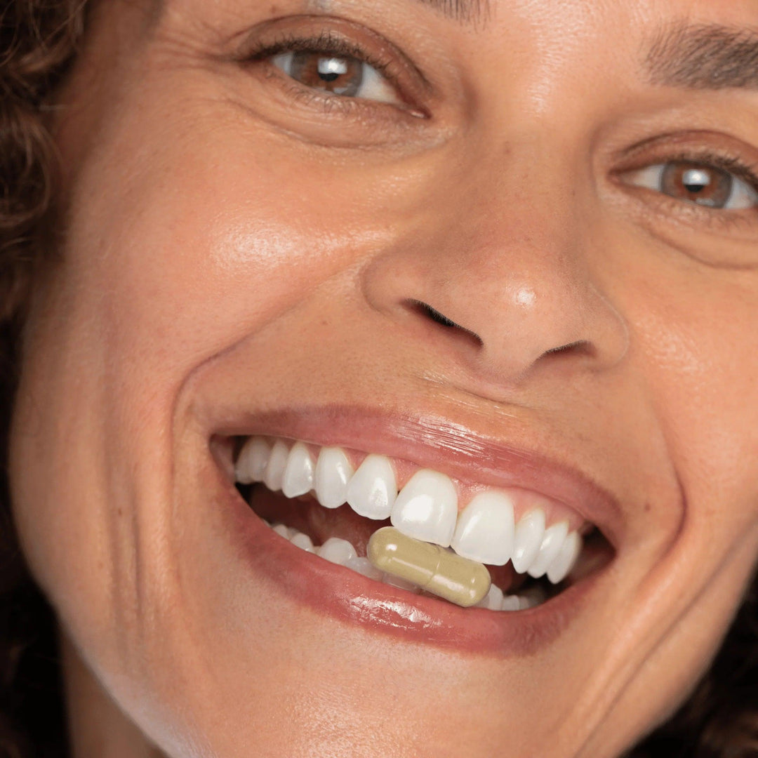 Close-up of smiling woman holding a capsule between her teeth, promoting the Keep it Cool menopause relief bundle.
